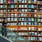 person going down an escalator with giant bookshelves in the background spanning both floors