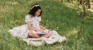 a Black woman reading on a blanket in a field