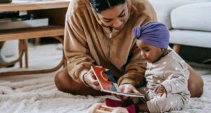 brown-skinned Black mother reading to her baby, who has a purple turban on